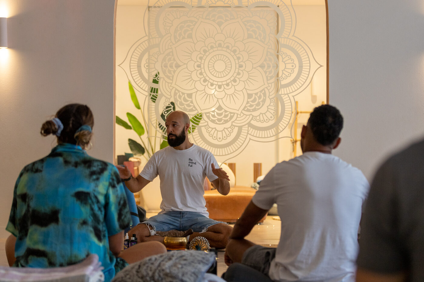 Participants sitting cross-legged in a circle facing Daniel Augustine at the front of a softly lit studio.