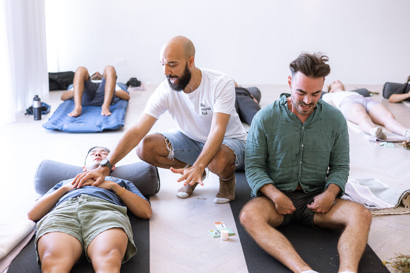 Daniel Augustine kneeling beside two participants in a breathwork session, guiding one who is lying down while the other sits cross-legged.